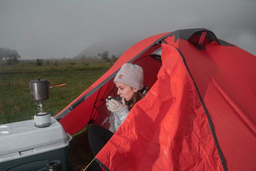 A female drinking coffee while sitting in a hiking tent on a foggy day