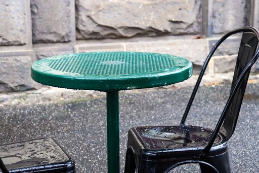 green table and black chair with raindrops after rain on pavement outside restaurant