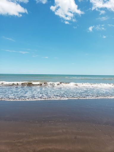 A beautiful shot of sea waves crashing on a sandy beach under a blue cloudy sky on a sunny day