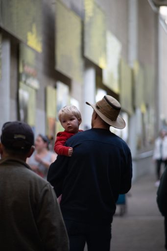 A Caucasian man with a cowboy hat carrying his son on the street