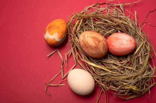 An overhead shot of colorful painted Easter eggs on straw nest with red copy space