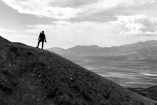 A grayscale shot of a man standing on a hill admiring the nature