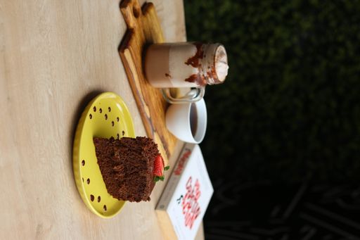 A chocolate cake with coffees and a book on a table in a coffee shop