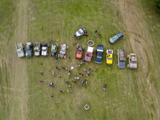 An aerial shot of lots of people near off-road vehicles in a grass field near trees