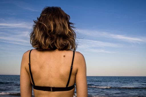 A brunette woman with a black bikini looking at the sea in cloudy sky background