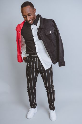 A vertical studio shot of an African American male model posing in fashionable clothes