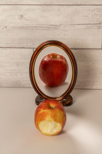 bitten red apple reflected in a mirror isolated on a white table with copy space