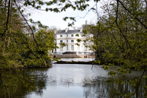 A beautiful shot of a white building behind a lake and trees