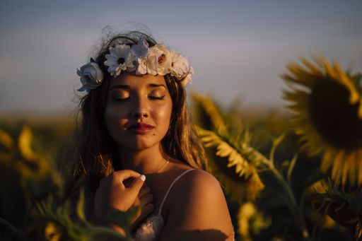 A young brunette female in a flower crown with closed eyes enjoying the sun in a sunflower field