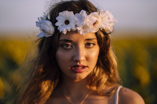 A  shallow focus portrait of young caucasian brunette female with flower crown looking into the camera with serious expression during golden hour