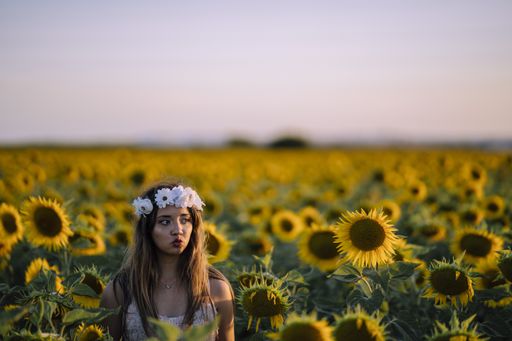 A young brunette female in a white flower crown looking to the side making a duck face in a sunflower field