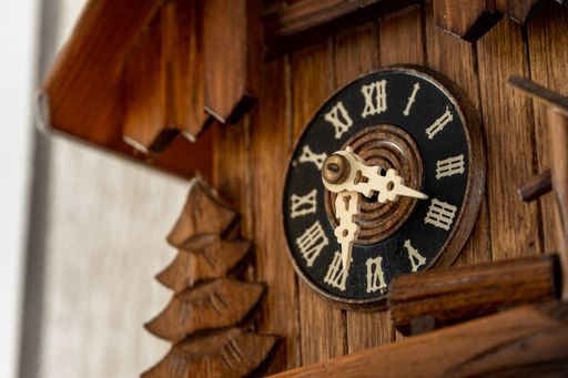 A closeup shot of a clock with Roman numbers on a wooden surface