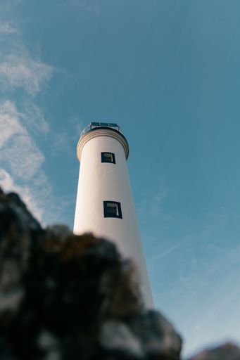 A low angle shot of a white lighthouse on a blue sky background