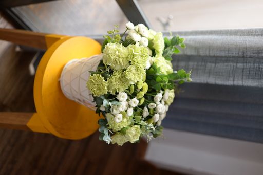 A vertical shot of a decorative vase with a green-white bouquet on a yellow stool