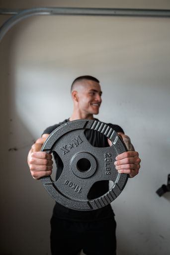 The vertical shot of an athlete man holding a rubber weight disc in his hand