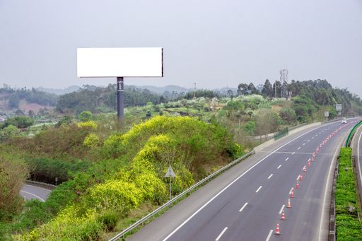 A blank billboard with copy space on a field near a highway