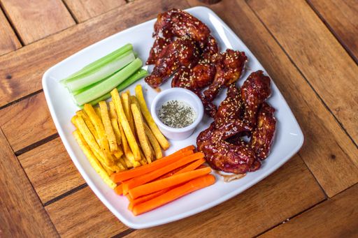 A closeup of fresh chicken wings with french fries and cut vegetables.