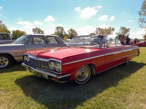 old popular red Chevrolet Chevy Impala SS Super Sport V8 two door convertible 1964 by GM in the countryside. Nature grass and trees. Classic car show