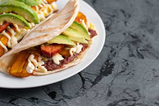 A closeup shot of a white plate with delicious Honduran baleadas on a black textured surface