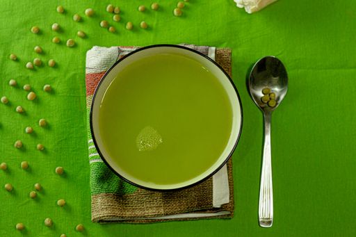 A high angle shot of a bowl of delicious green pea soup on a green surface