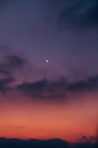 A vertical shot of a crescent moon in a bright sunset sky