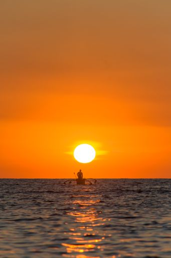 A vertical shot of a silhouette of a person on a boat on the sea at sunset