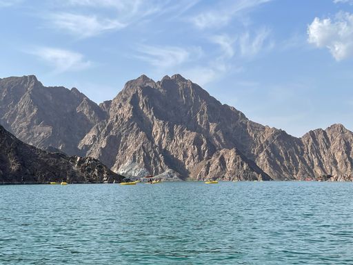 A beautiful landscape view of Hatta Lake and Hajar Mountains in bright sunlight against blue sky in Emirate of Dubai, United Arab Emirates