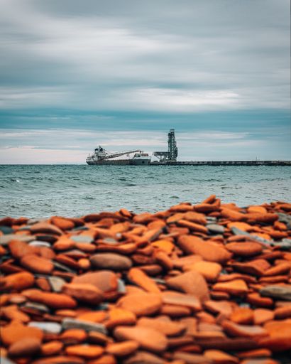 A vertical shot of pebbles on a beach with a ship in the background
