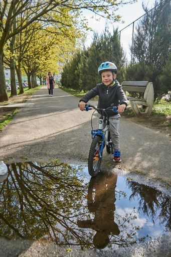 A young boy with a safety helmet sitting on a bicycle by a rain puddle in the Orla Bialego area
