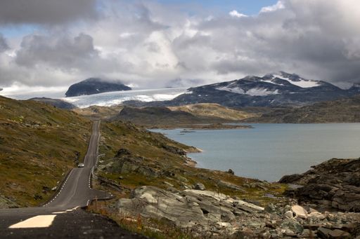 A long road on route 55 surrounded by a big lake and snowy mountains and a cloudy sky