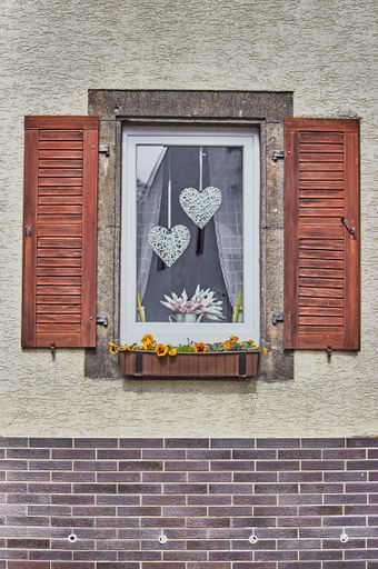 A beautiful exterior old brick wall with a window and plants in the old village of Monreal, Germany