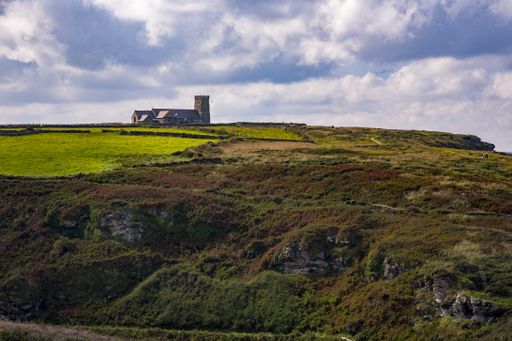 The Brentor Church on a hill covered in greenery under a blue cloudy sky in Devon, the UK