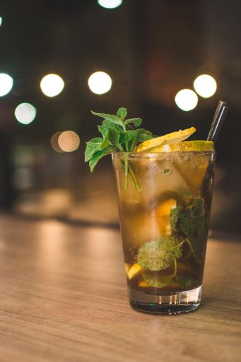 A cold beverage with ice cubes, lemon slices, mint leaves and a black straw
