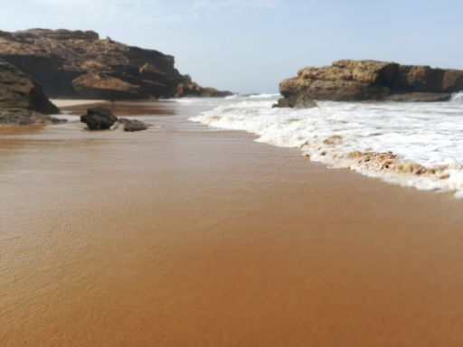 A closeup of sea waves on the sandy beach with stones in Morocco