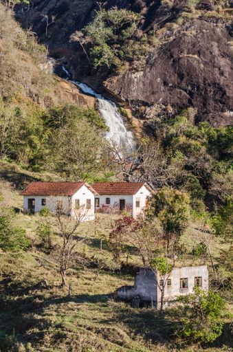 A vertical shot of small houses in the forest with a waterfall on the background