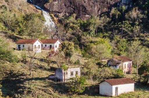An aerial shot of small houses in the forest with a waterfall on the background
