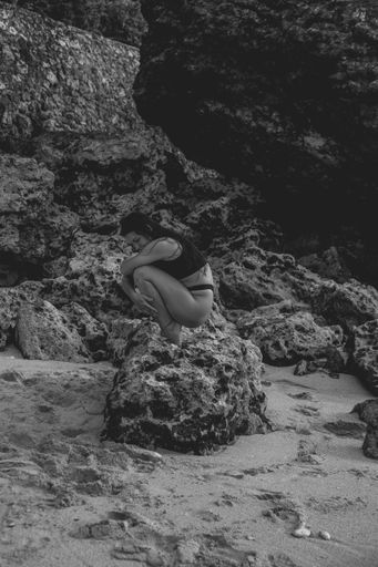Young European woman in black bikini sitting on rocks,  black and white photo, body aesthetics