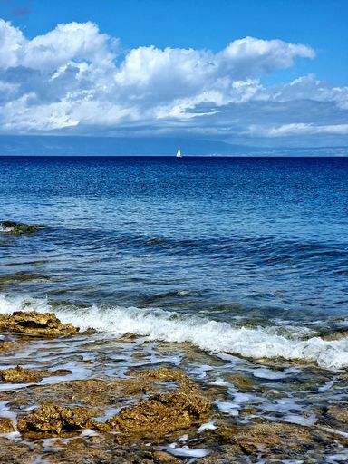 A vertical shot of a blue sea with a boat sailing far away, under a cloudy sky