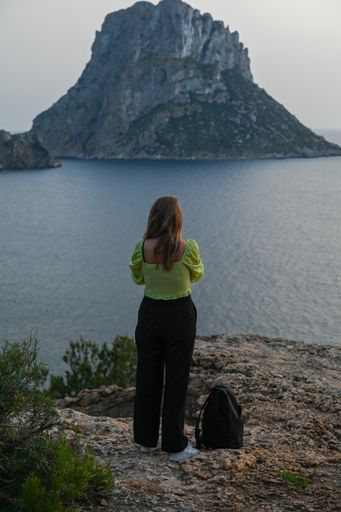 A young female wearing a green top facing the Es Vedra viewpoint in Ibiza, Spain.