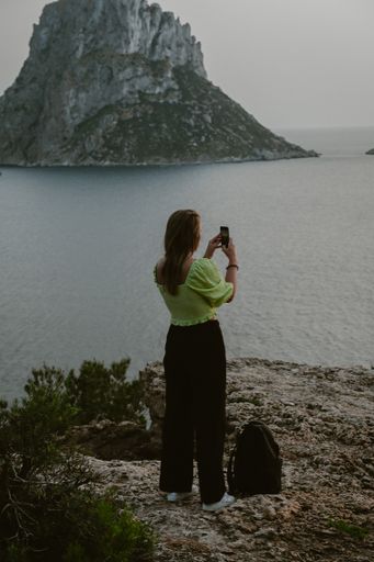 A young woman taking pictures with her mobile phone at the Es Vedra viewpoint in Ibiza, Spain.