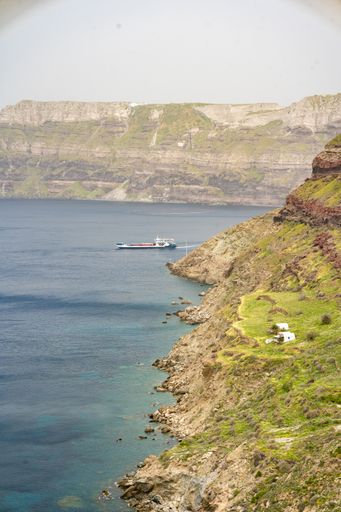 A vertical shot of Santorini hillside near the Aegean sea, with a boat sailing on the water