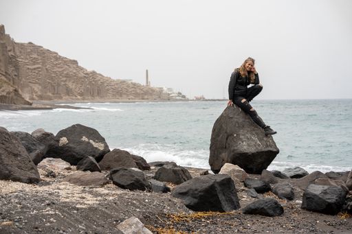A Caucasian young woman sitting on a rock by the Aegean sea, Santorini