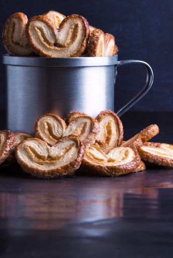 A vertical shot of heart-shaped palmier pastries in and around a silver jug
