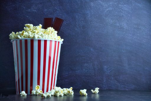 A bucket of popcorn with film strips on a blue background with copy space