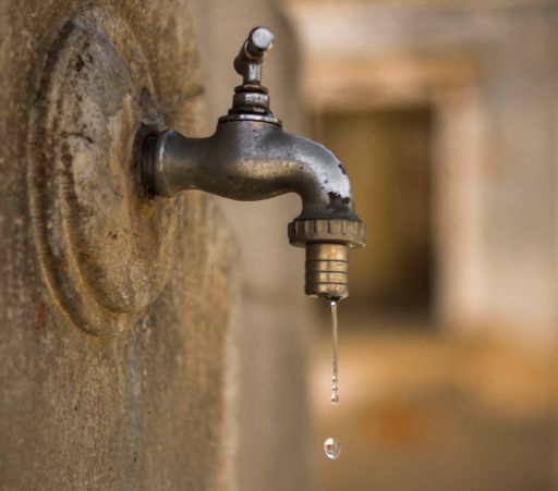 A closeup shot of a dripping iron faucet on a stone wall