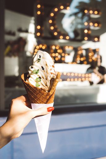 A vertical shallow focus shot of a young female hand holding soft serve ice cream with green flakes in a cone