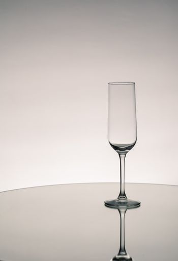 A grayscale shot of an empty glass cup with reflection on a mirror surface
