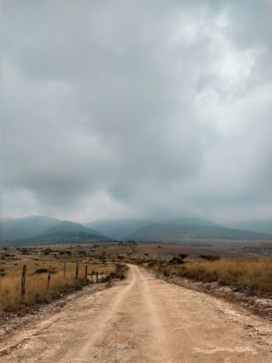 A vertical shot of a brown road leading to distant misty hills