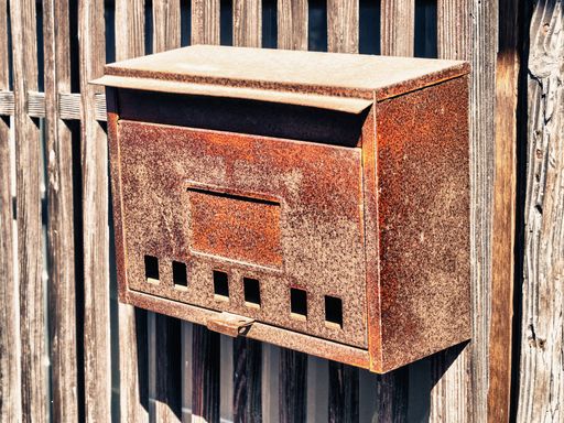 A closeup of an old rusty mailbox on a wooden gate