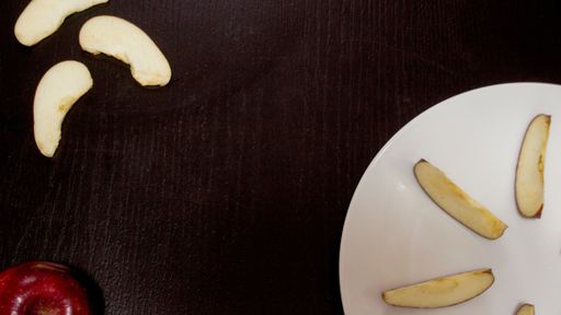 An overhead shot of two apple slices on a brown surface next to a white plate with two apple slices